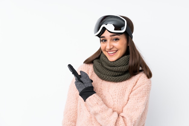 Narciarz dziewczyna w okularach snowboardowych na pojedyncze białej ścianie, wskazując na bok, aby przedstawić produkt