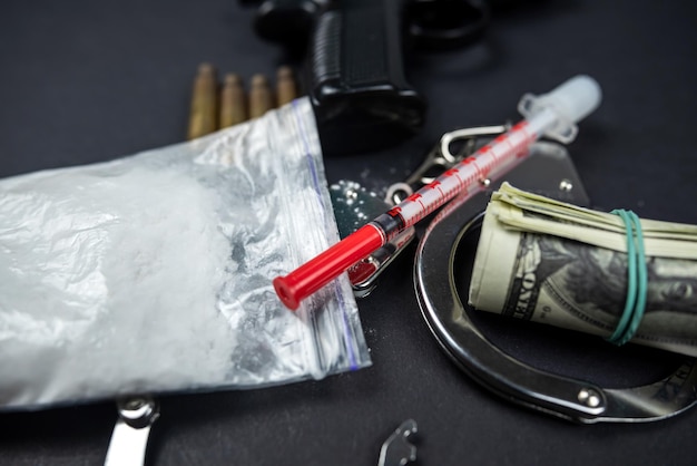 Zdjęcie narkotyki i pistolet na pieniądze z tłumikiem i kajdankami odizolowanymi na czarnym stole
