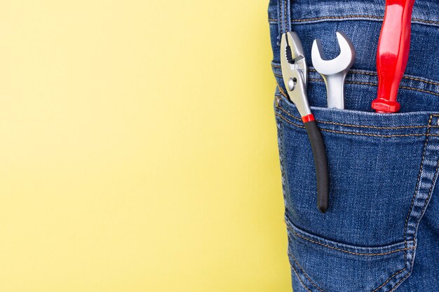 Narzędzia w kieszeni jeansów rzemieślnika na żółtej ścianie z miejscem na tekst