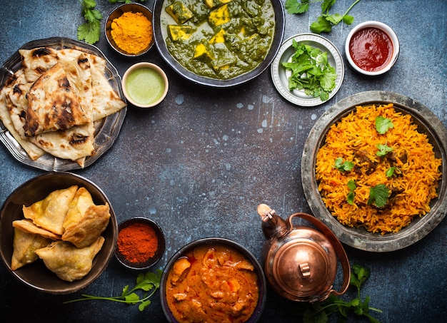 Narzut tradycyjnych indyjskich potraw i przystawek: curry z kurczaka, pilaw, chleb naan, samosy, paneer, chutney na rustykalnym tle. Stół z wyborem potraw kuchni indyjskiej, miejsce na tekst