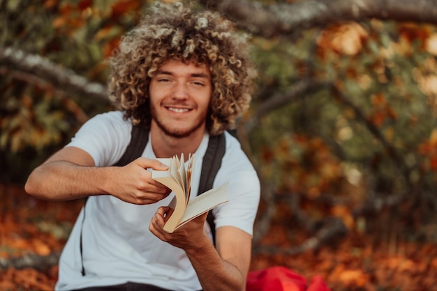 Nastolatek afro relaksuje się czytając książkę siedząc w lesie przy pięknej jesiennej pogodzie