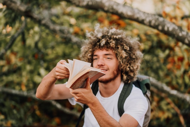 Nastolatek afro relaksuje się czytając książkę siedząc w lesie przy pięknej jesiennej pogodzie