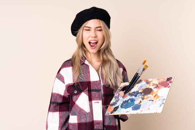 Nastolatek artysty dziewczyna trzyma paletę na niebieską ścianą krzyczy do przodu z szeroko otwartymi ustami