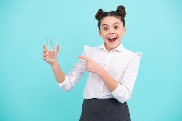 Nastolatek dziewczyna pije wodę ze szkła na niebieskim tle Życie codzienne zdrowie Pij wodę dla zdrowia i równowagi ciała Spragnione dziecko odwodnienia Zdumiony nastolatek Podekscytowana nastolatka