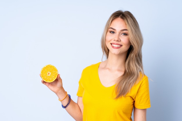 Nastolatek dziewczyna trzyma pomarańcze odizolowywająca na błękit ścianie ono uśmiecha się dużo