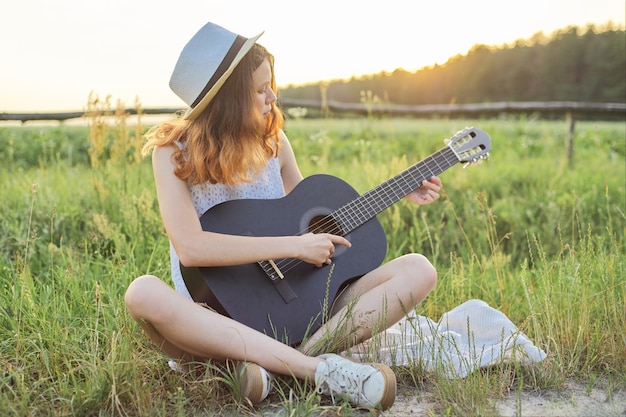 Nastolatek dziewczyna w kapeluszu bawić się gitary natury tło