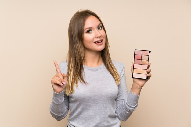 Nastolatek dziewczyna wskazuje w górę doskonałego pomysłu z makeup paletą nad odosobnionym tłem