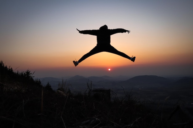 Zdjęcie nastolatek i sportowiec skaczący na pni drzewa i robiący skok na skrzydłach przy zachodzie słońca
