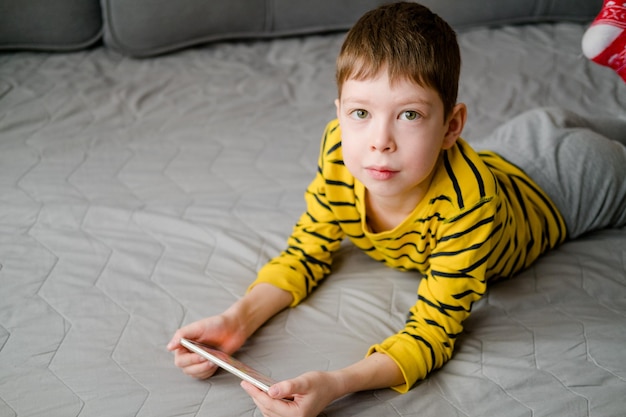 Nastolatek leży na kanapie z telefonem w rękach Dziecko bawi się w domu w telefonie Wypoczynek z telefonem Wakacje z gadżetami