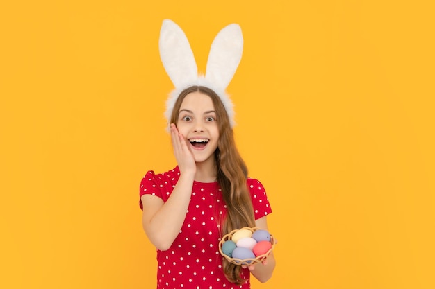 Nastolatek nosi uszy królika i trzyma kolorowe pisanki odizolowane na żółtym tle Zdumiony zaskoczony emocjami młodej nastolatki