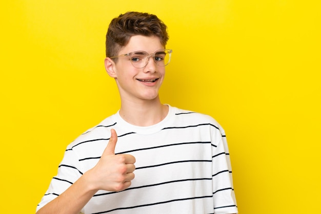 Nastolatek Rosjanin odizolowany na żółtym tle W okularach i kciukiem do góry