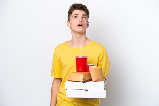 Nastolatek Rosjanin trzymający fast food na białym tle patrząc w górę i z zaskoczonym wyrazem twarzy