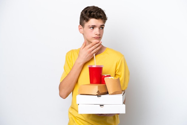 Nastolatek Rosjanin trzymający fast food na białym tle patrząc w górę podczas uśmiechania się