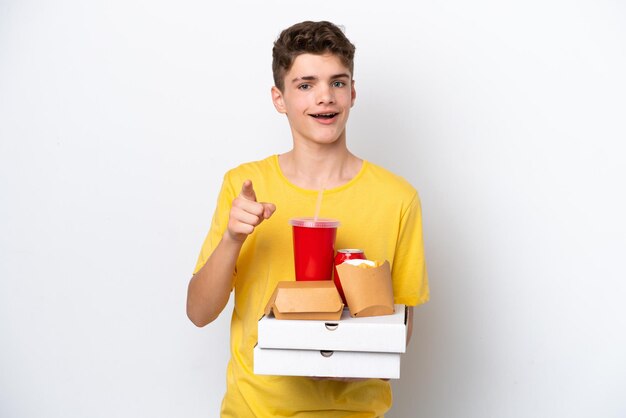 Nastolatek Rosjanin trzymający fast food na białym tle zaskoczony i wskazujący przód