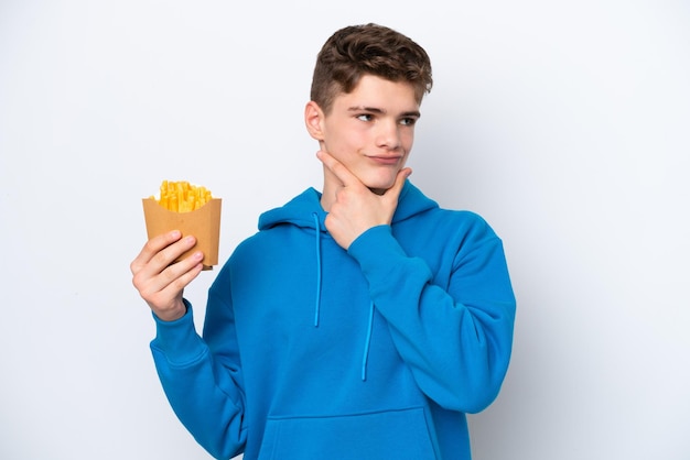 Nastolatek Rosjanin trzymający smażone ziemniaki na białym tle mający wątpliwości