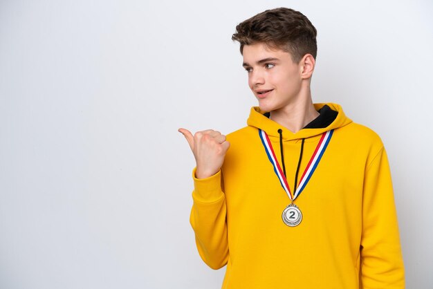 Nastolatek Rosjanin z medalami na białym tle wskazujący na bok, aby zaprezentować produkt