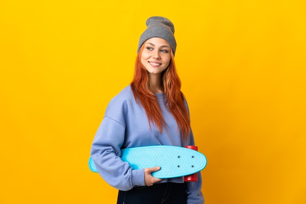 Nastolatek rosyjski skater dziewczyna na białym tle na żółtym tle, patrząc z boku i uśmiechnięty