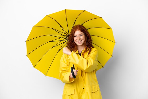 Nastolatek rudowłosa dziewczyna przeciwdeszczowy płaszcz i parasol na białym tle świętuje zwycięstwo