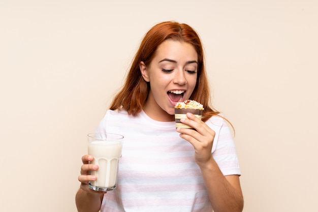 Nastolatek rudzielec dziewczyna trzyma szkło mleko i słodka bułeczka nad odosobnionym