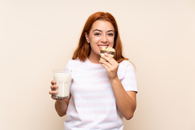 Nastolatek rudzielec dziewczyna trzyma szkło mleko i słodka bułeczka nad odosobnionym