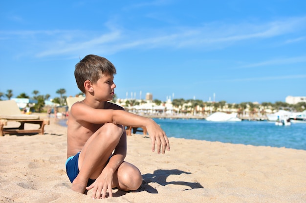 Nastolatek siedzi na plaży i patrzy na morze