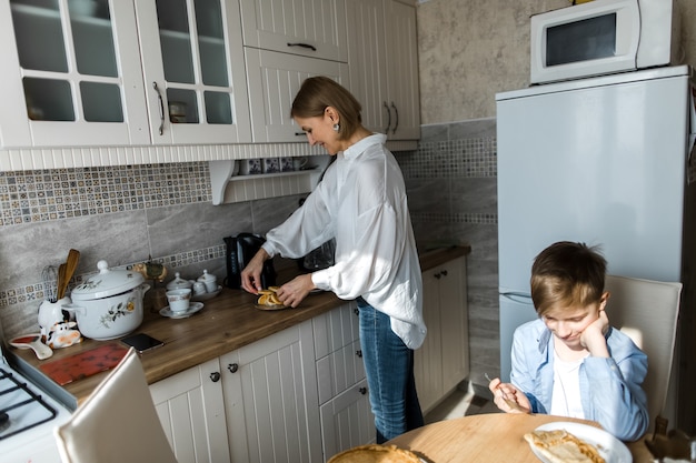 Zdjęcie nastolatek siedzi w kuchni przy stole na tle kobieta przygotowuje jedzenie.