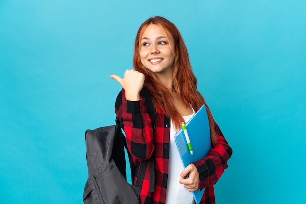 Nastolatek student Rosjanka na białym tle na niebieskiej ścianie, wskazując w bok, aby przedstawić produkt