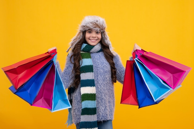 Nastolatek w czapce zimowej trzyma torbę na zakupy, ciesząc się sprzedażą Dziewczynka jest gotowa na zakupy Szczęśliwa twarz pozytywne i uśmiechnięte emocje nastolatki
