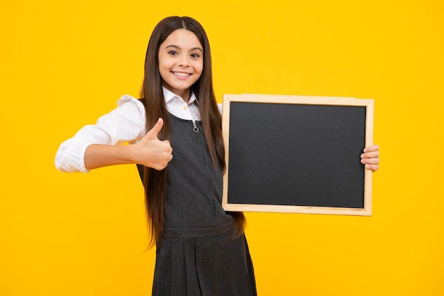 Nastolatek younf school girl trzymając pustą tablicę w szkole odizolowany na żółtym tle Portret nastoletniej studentki Szczęśliwa dziewczyna twarz pozytywne i uśmiechnięte emocje