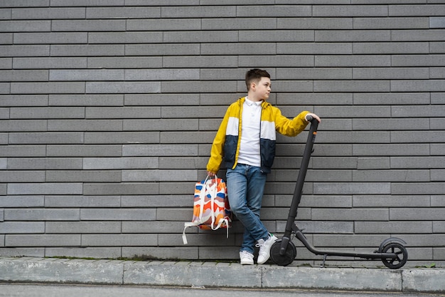 Nastolatek z plecakiem i skuterem elektrycznym na tle ceglanego muru