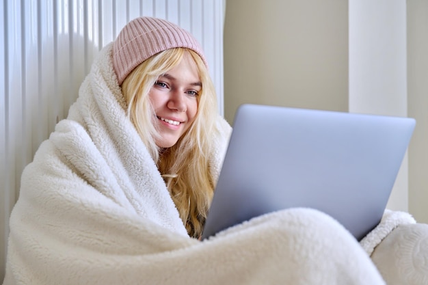Nastolatek zamrożony w zimie rozgrzewa się czapką z koca patrząc na laptopa