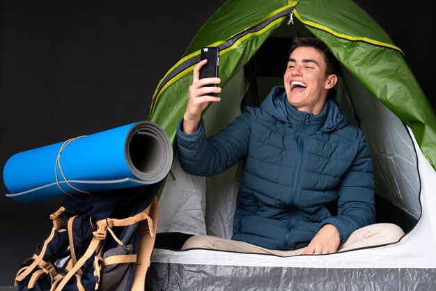 Nastolatka Caucasian Mężczyzna Wśrodku Campingowego Zielonego Namiotu Odizolowywającego Na Czarnym Tle Robi Selfie