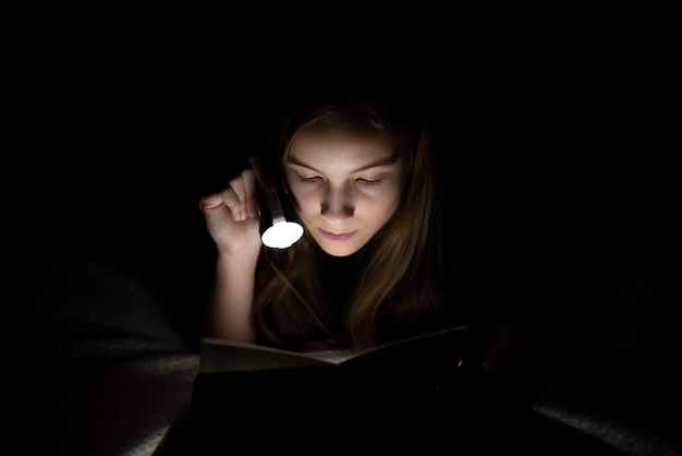 Nastolatka czyta w ciemności z latarką