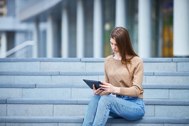 Nastolatka kobieta siedzi na schodach, korzysta z tabletu w słoneczny letni dzień copyspace