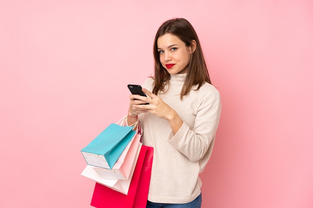 Nastolatka na różowym gospodarstwa torby na zakupy i pisanie wiadomości ze swoim telefonem komórkowym do przyjaciela