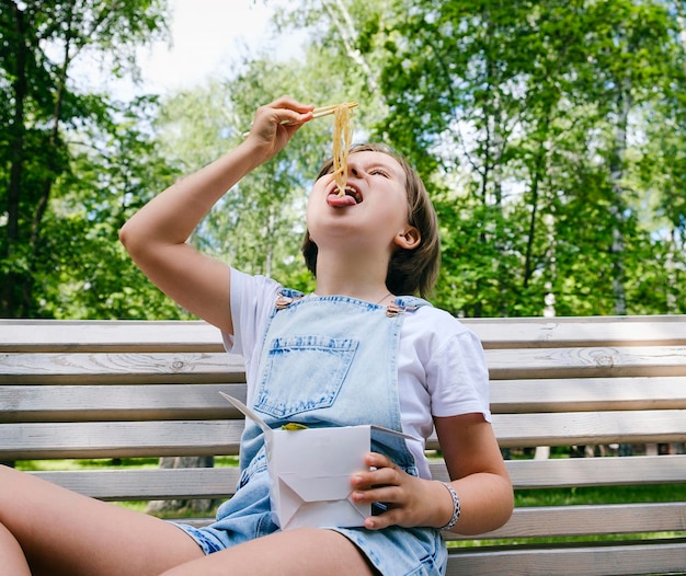 Nastolatka na spacerze w letni dzień w parku je lunch z wokiem z makaronem