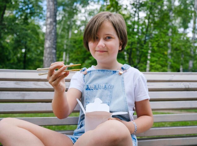 Nastolatka na spacerze w letni dzień w parku je lunch z wokiem z makaronem