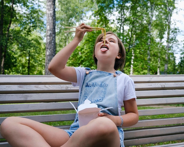 Nastolatka na spacerze w letni dzień w parku je lunch z wokiem z makaronem