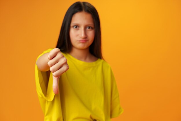 Zdjęcie nastolatka pokazuje gest kciuka w dół na żółtym tle