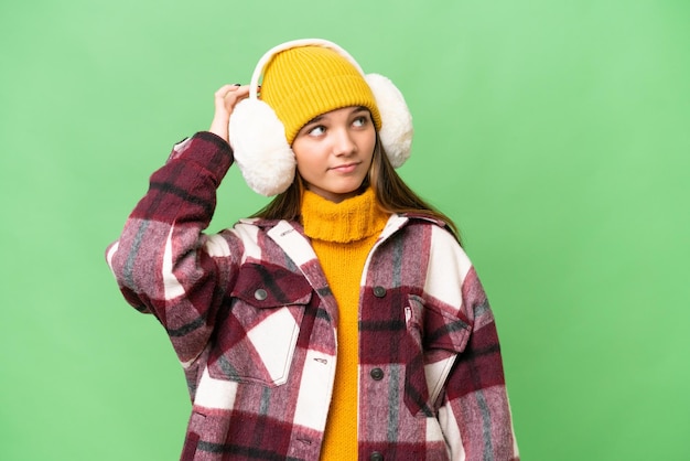 Nastolatka rasy kaukaskiej w zimowych mufkach na odosobnionym tle, mająca wątpliwości i zdezorientowany wyraz twarzy