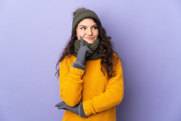 Nastolatka Rosjanka z czapka zimowa na białym tle na fioletowej ścianie myśli pomysł patrząc w górę