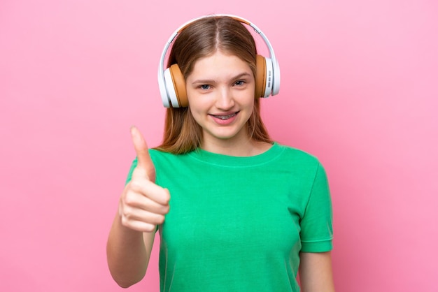 Nastolatka rosyjska dziewczyna odizolowana na różowym tle słuchająca muzyki i z kciukiem do góry