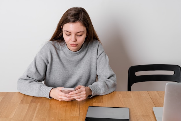 Nastolatka siedzi przy drewnianym stole i zwleka w mediach społecznościowych. Problem uzależnienia