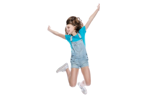 Zdjęcie nastolatka skacze dziecko w denim kombinezon i niebieski tshirt radość z działalności i pozytywne pojedynczo na białym tle