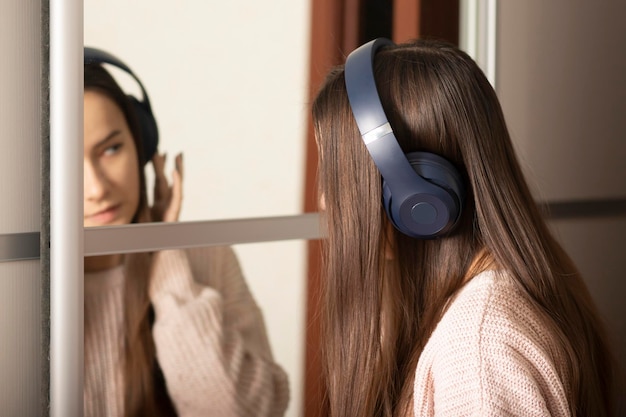 Nastolatka słuchająca muzyki w domu przed lustrem w słuchawkach bezprzewodowych