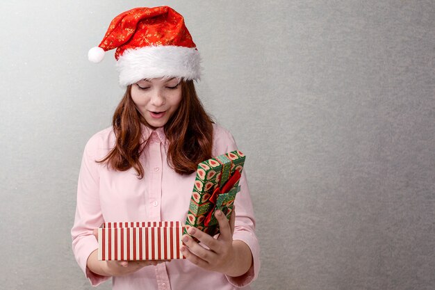 Nastolatka stoi w domu w czapce Mikołaja i otwiera świąteczny prezent.