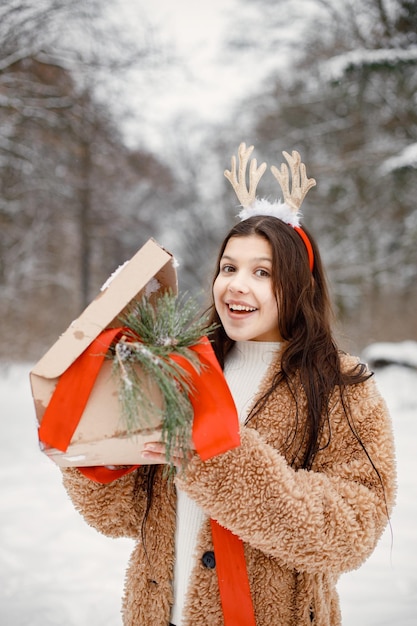 Nastolatka stojąca w parku zimowym z pudełkiem na prezent