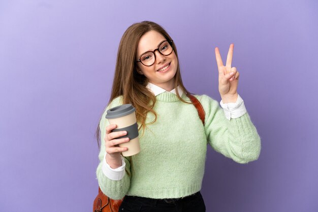 Nastolatka studentka na odosobnionym fioletowym tle uśmiecha się i pokazuje znak zwycięstwa