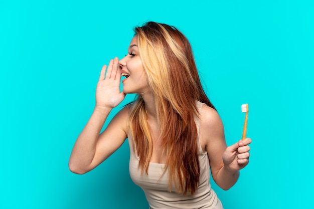 Nastolatka szczotkująca zęby na odosobnionym niebieskim tle, krzycząca z szeroko otwartymi ustami
