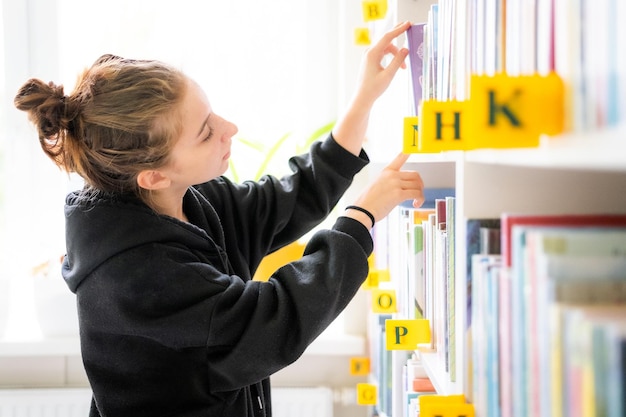 Nastolatka szuka odpowiedniej książki w szkolnej bibliotece